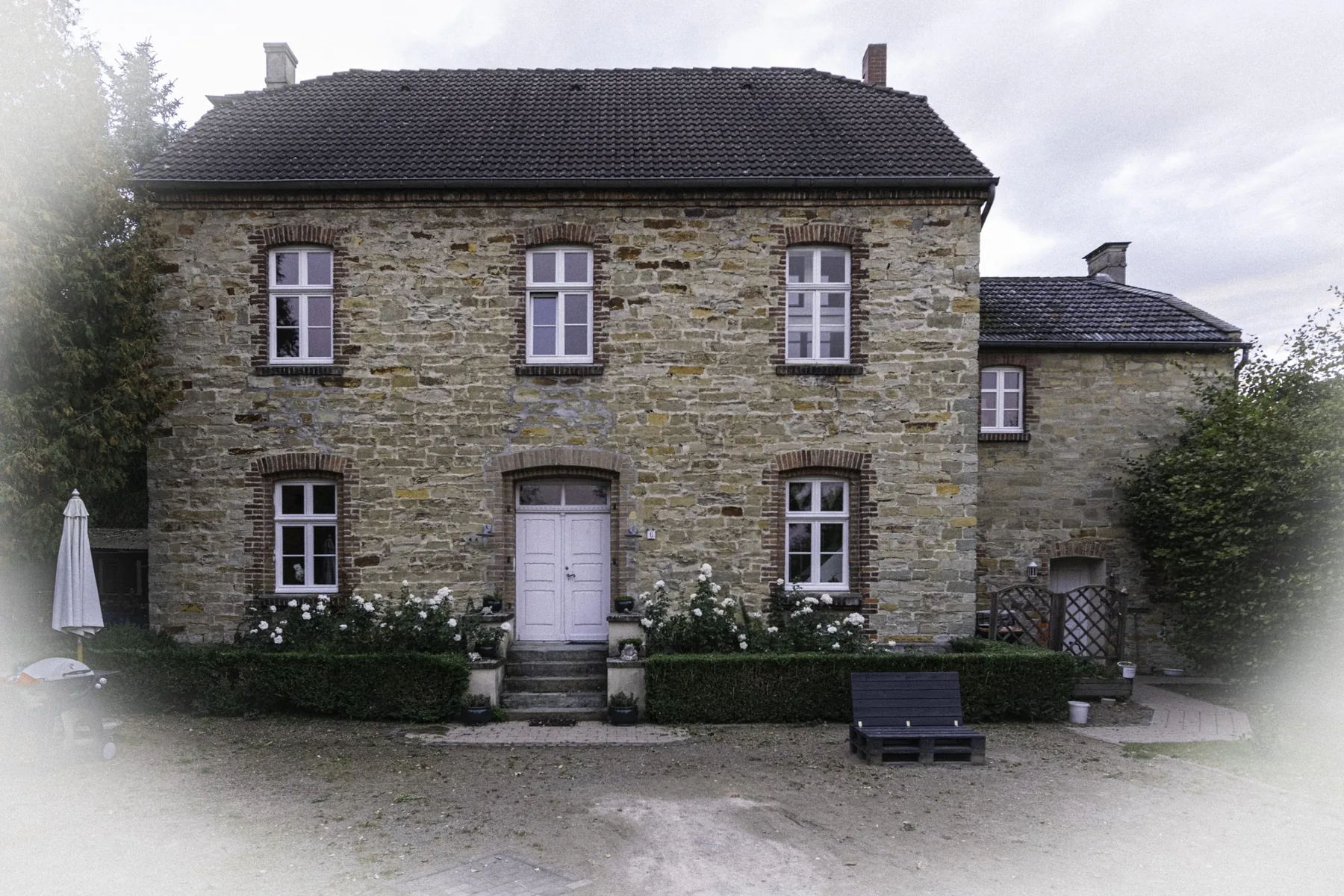 Die Kaplanei: zweigeschossiges Bruchsteinhaus mit heller Tür und Blumenkästen vor den Fenstern