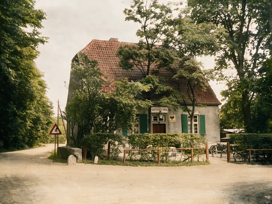 Farbige Aufnahme des Gasthauses mit den Schildern „Gaststätte Krug“ und „Poststelle“, davor ein Zaun und abgestellte Fahrräder